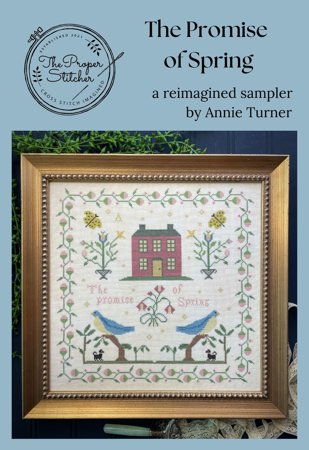 Framed cross-stitch sampler titled 'The Promise of Spring' by Annie Turner on a blue background.