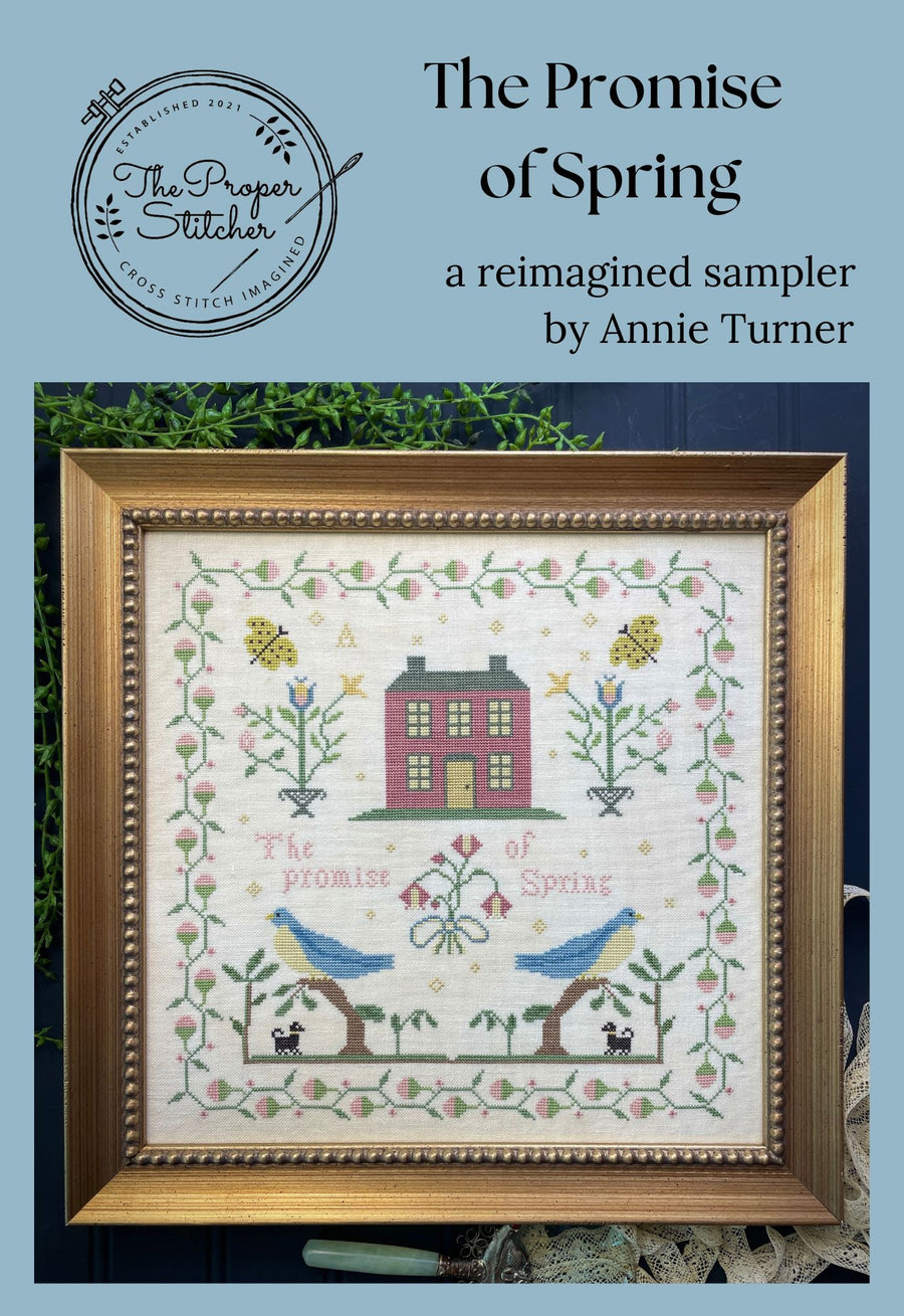 Framed cross-stitch sampler titled 'The Promise of Spring' by Annie Turner on a blue background.