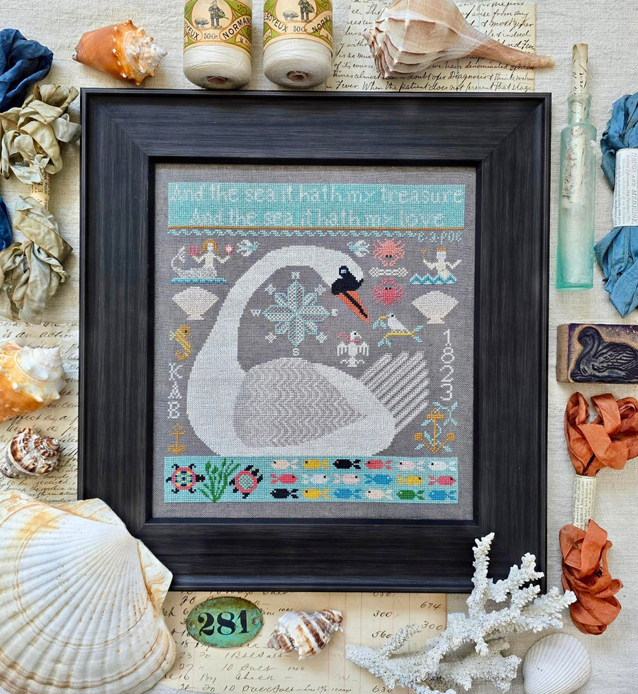 Framed cross-stitch art of a swan surrounded by seashells and nautical elements.