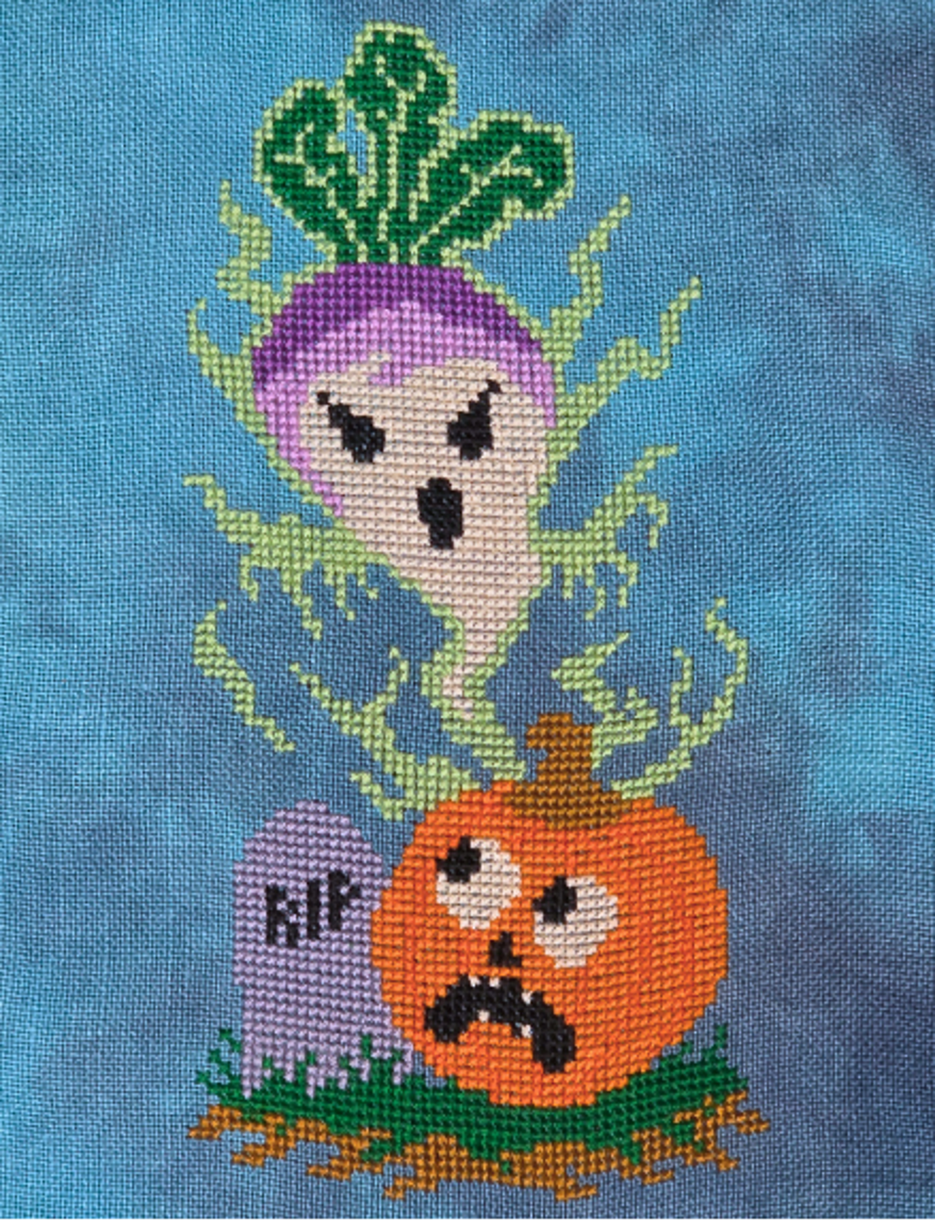 A close-up of a blue fabric surface featuring a stitched or embroidered Halloween design with a purple ghost, an orange jack-o'-lantern, green vines, and a small tombstone marked 'RIP'.