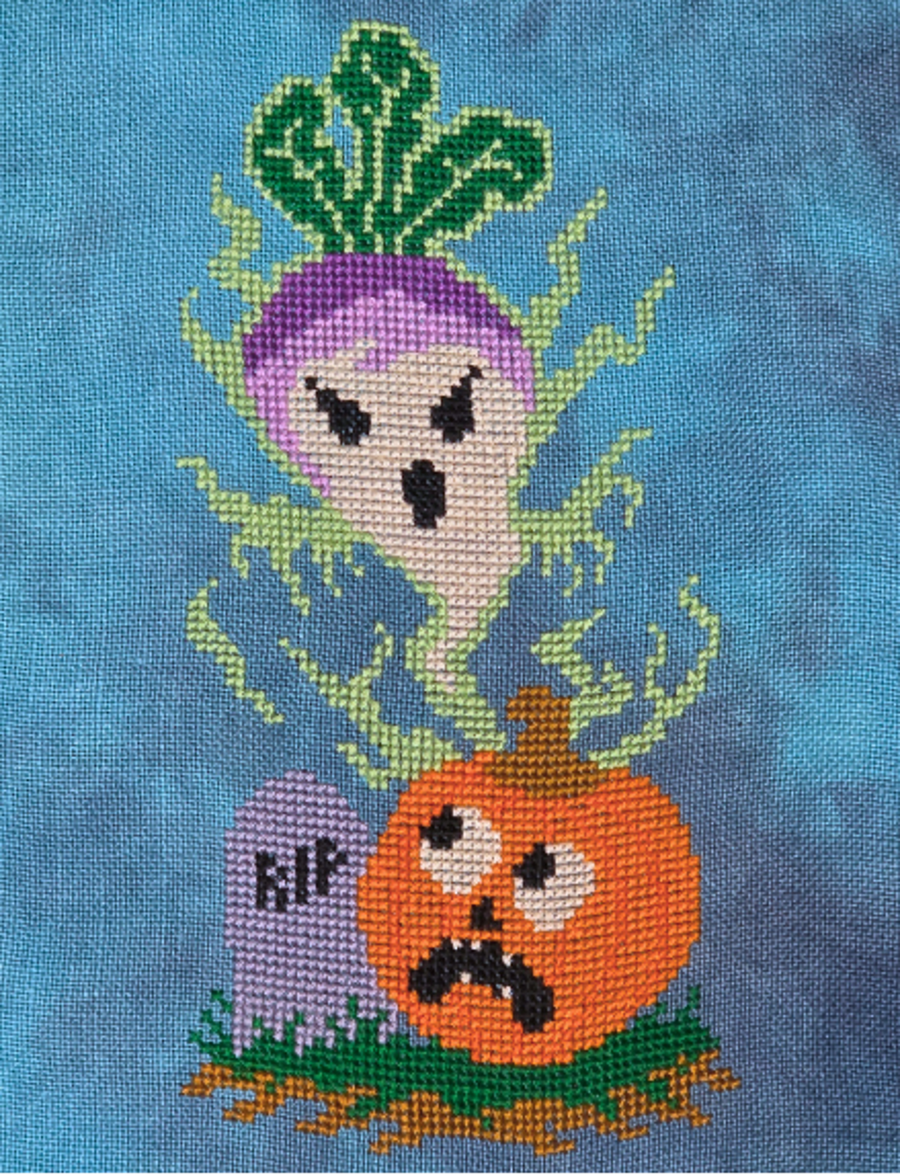 A close-up of a blue fabric surface featuring a stitched or embroidered Halloween design with a purple ghost, an orange jack-o'-lantern, green vines, and a small tombstone marked 'RIP'.