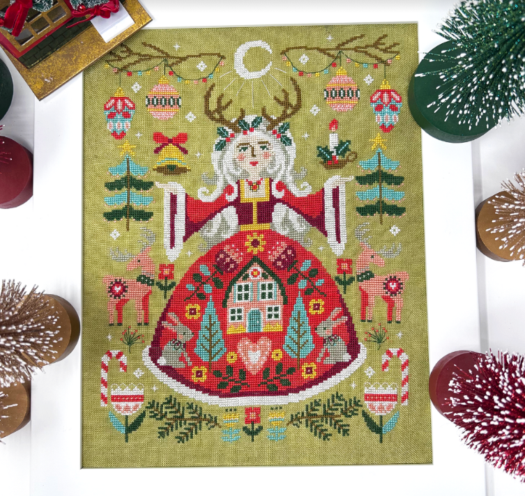 A colorful cross-stitch depiction of a Christmas themed scene with a figure resembling a goddess, antlers, and winter elements on a green background.