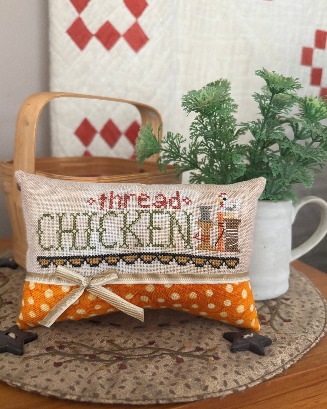 Decorative pillow with cross-stitched text and polka dot pattern on a table with a quilted backdrop.