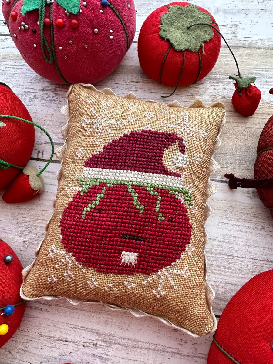 Cross-stitch needlework depicting a tomato dressed as Santa Claus, surrounded by other tomato-shaped ornaments.