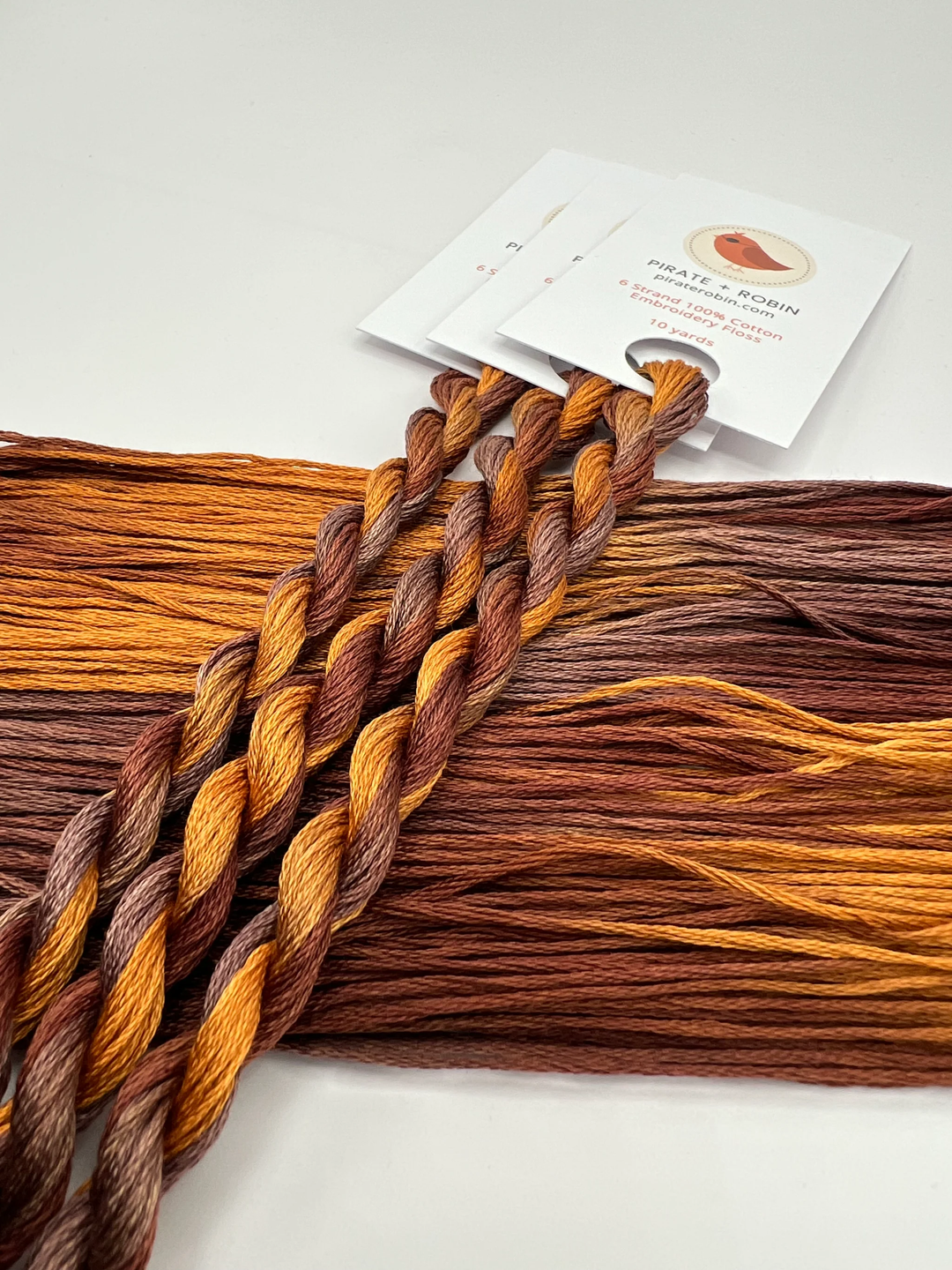 Three braided skeins  in brown and orange tones on a white background with a product card.