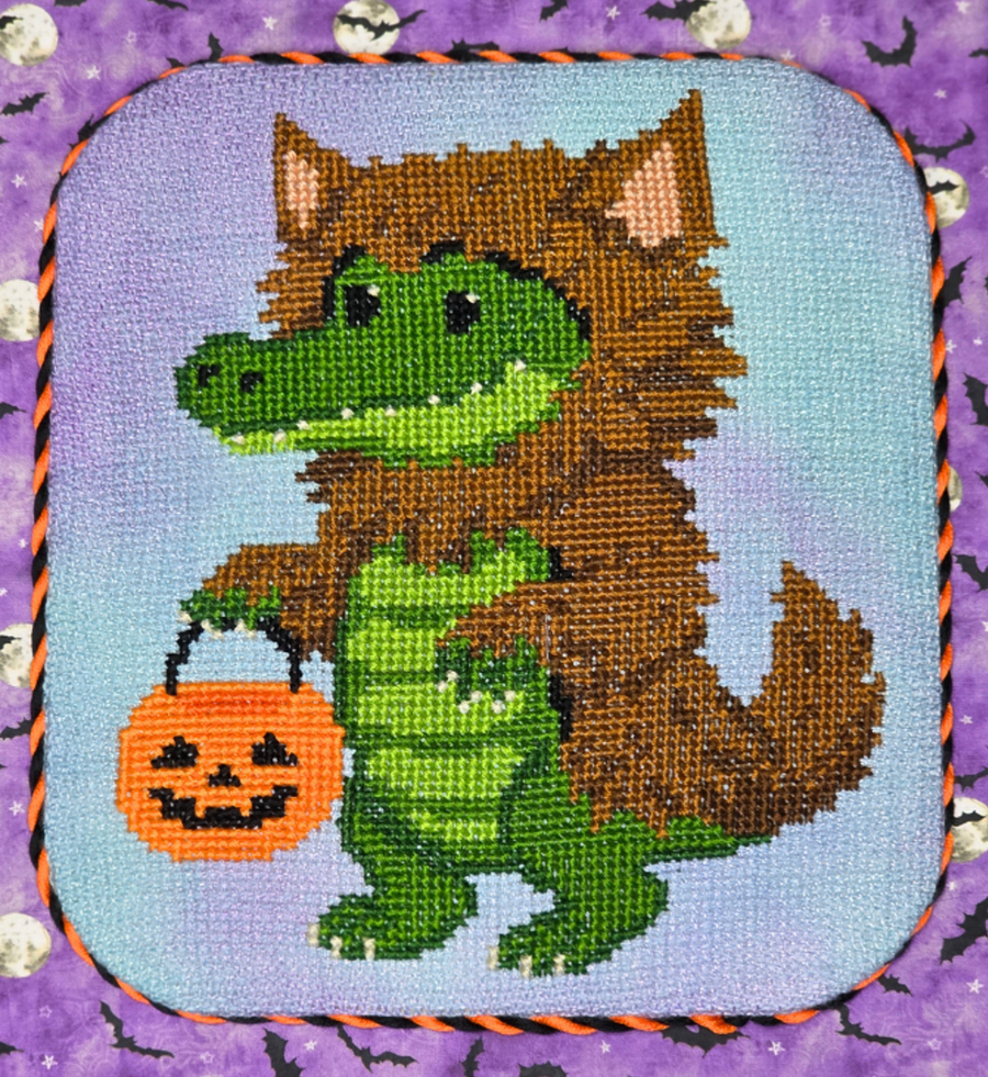 A square needlepoint canvas featuring a cartoon crocodile dressed as a werewolf, holding an orange jack-o'-lantern bucket. The werewolf has brown fur and pink ears, set against a light blue background.