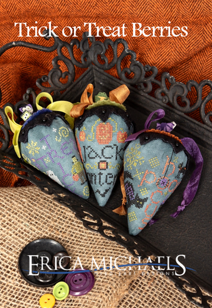 Three embroidered cross-stitch pincushions shaped like autumn berries in a decorative black tray, with the title 'Trick or Treat Berries' at the top and 'ERICA MICHAELS' branding at the bottom.