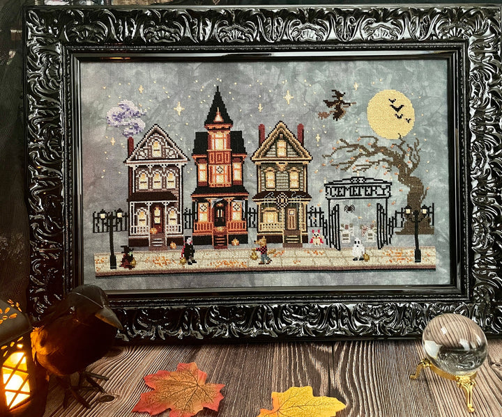Framed artwork of a Halloween-themed village scene with ornate black frame.