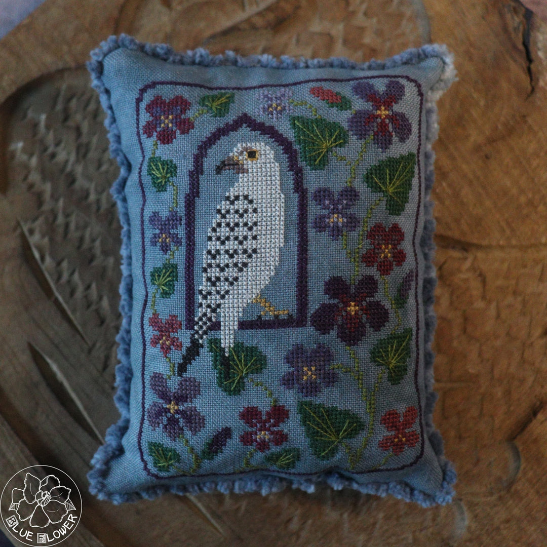 Embroidered pillow with a bird design and floral patterns on a wooden surface.