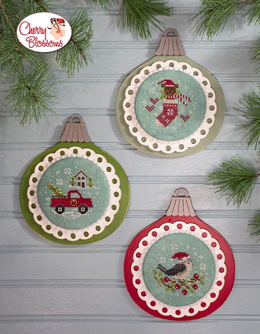 Three festive Christmas ornaments with embroidered designs on a wooden surface with pine branches.