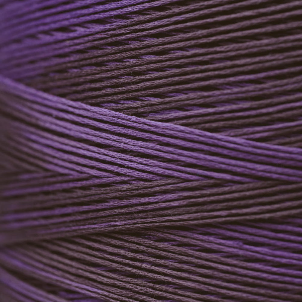 A close-up of tightly wound thread in a deep purple color, filling the entire frame.