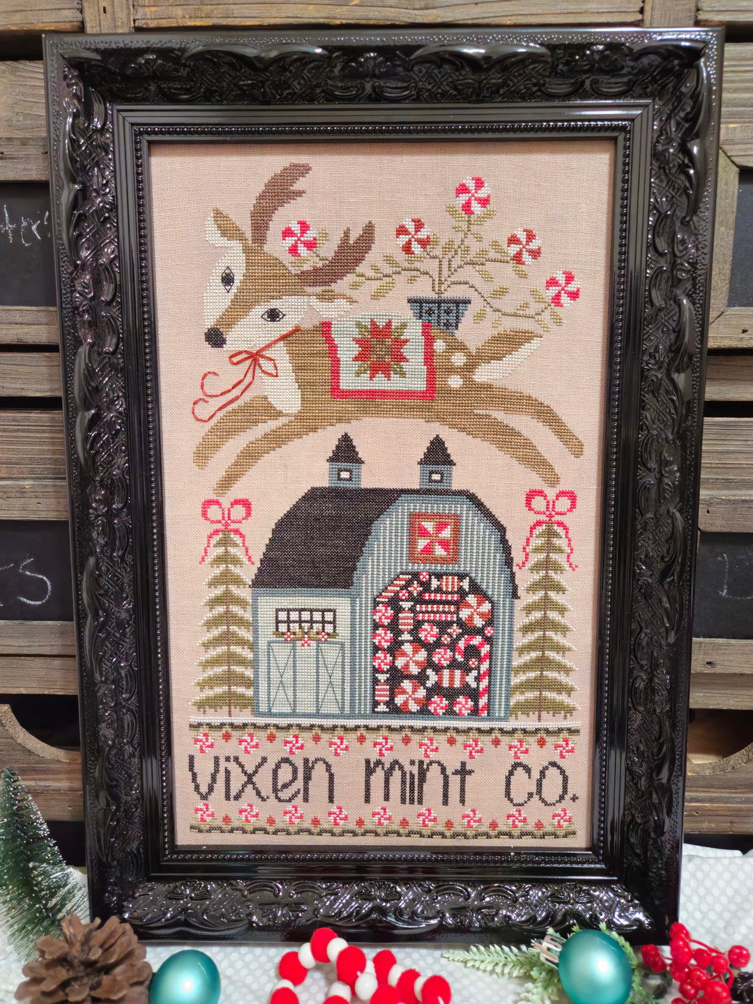 Framed cross-stitched picture of a deer with a barn and candy canes, featuring 'Vixen Mint Co.'