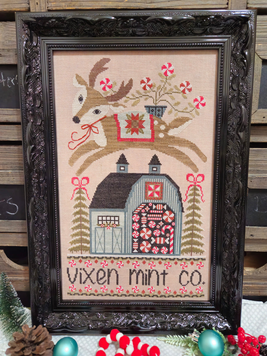 Framed cross-stitched picture of a deer with a barn and candy canes, featuring 'Vixen Mint Co.'