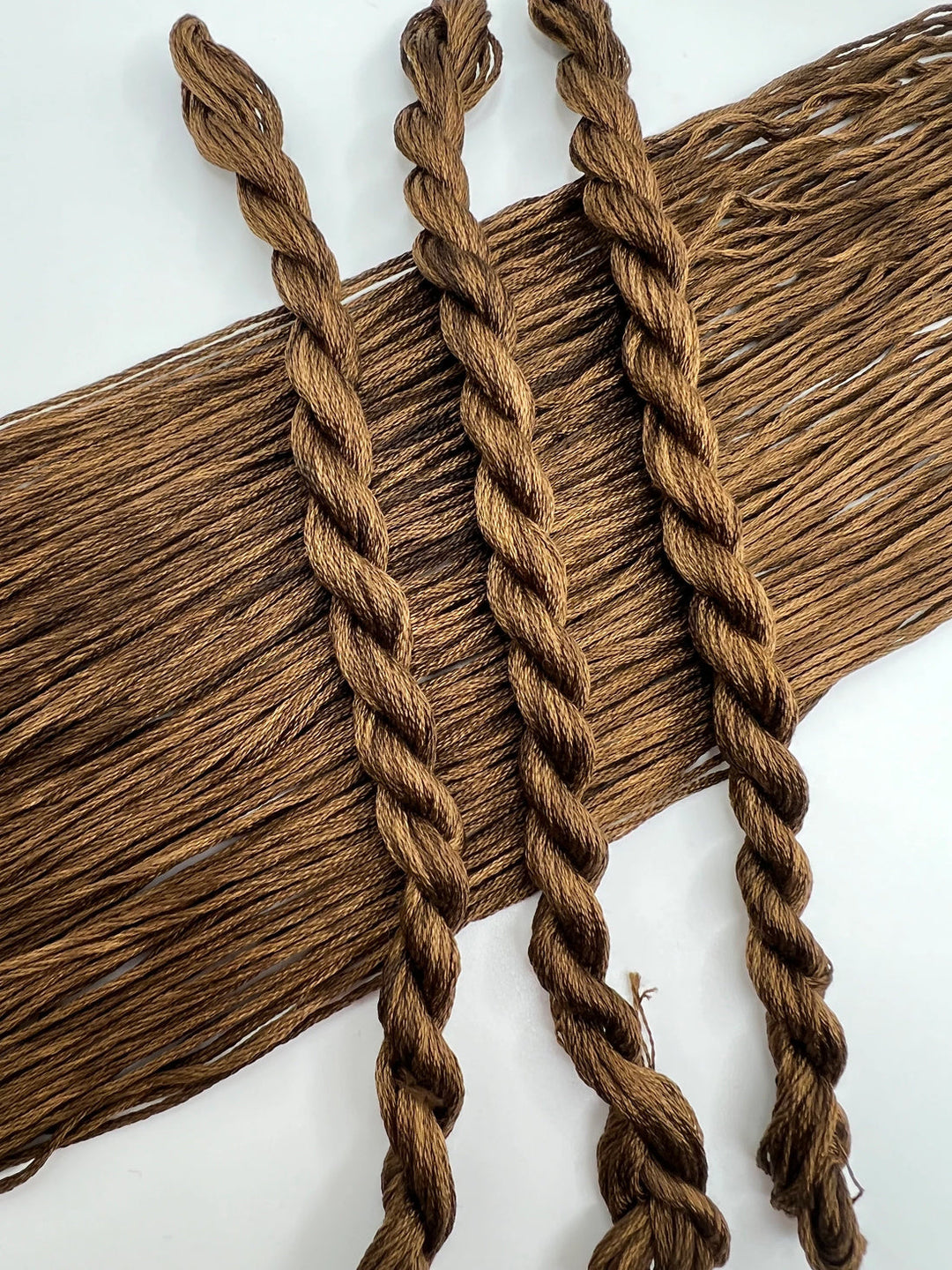 Three braided strands of brown yarn on a white background