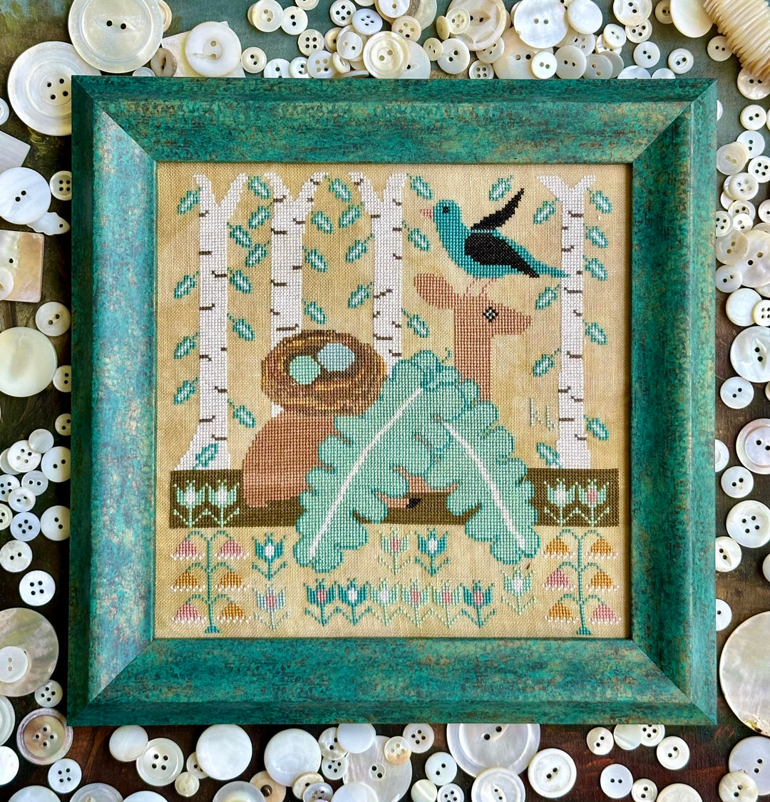 Framed cross-stitched artwork with a deer, bird, and nest design, surrounded by buttons.
