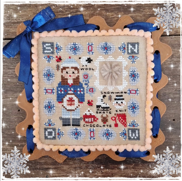 A square cross-stitch sampler featuring a winter snowman design, surrounded by a scalloped peach border and decorated with blue ribbons. The sampler is displayed on a rustic wooden background with a decorative scalloped wooden frame and white snowflake graphics.