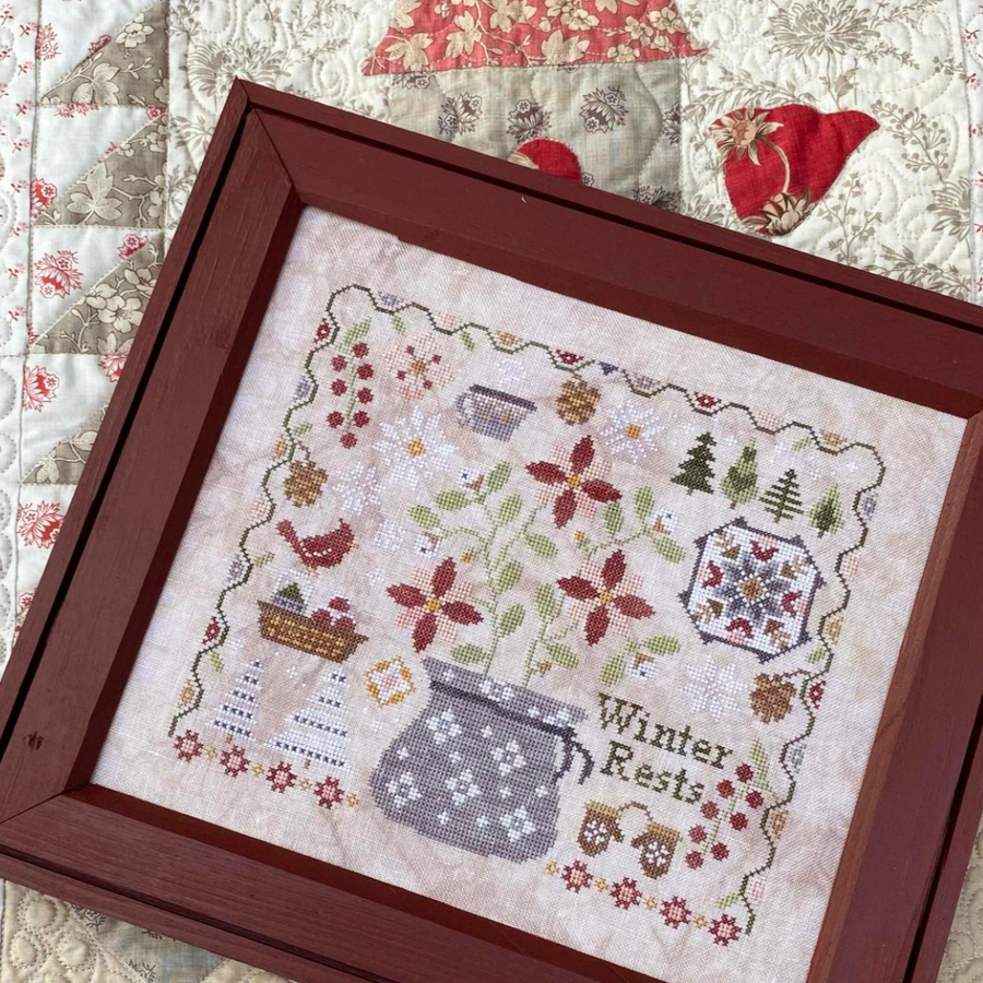 Framed cross-stitched piece with 'Winter Rests' text on a quilted background