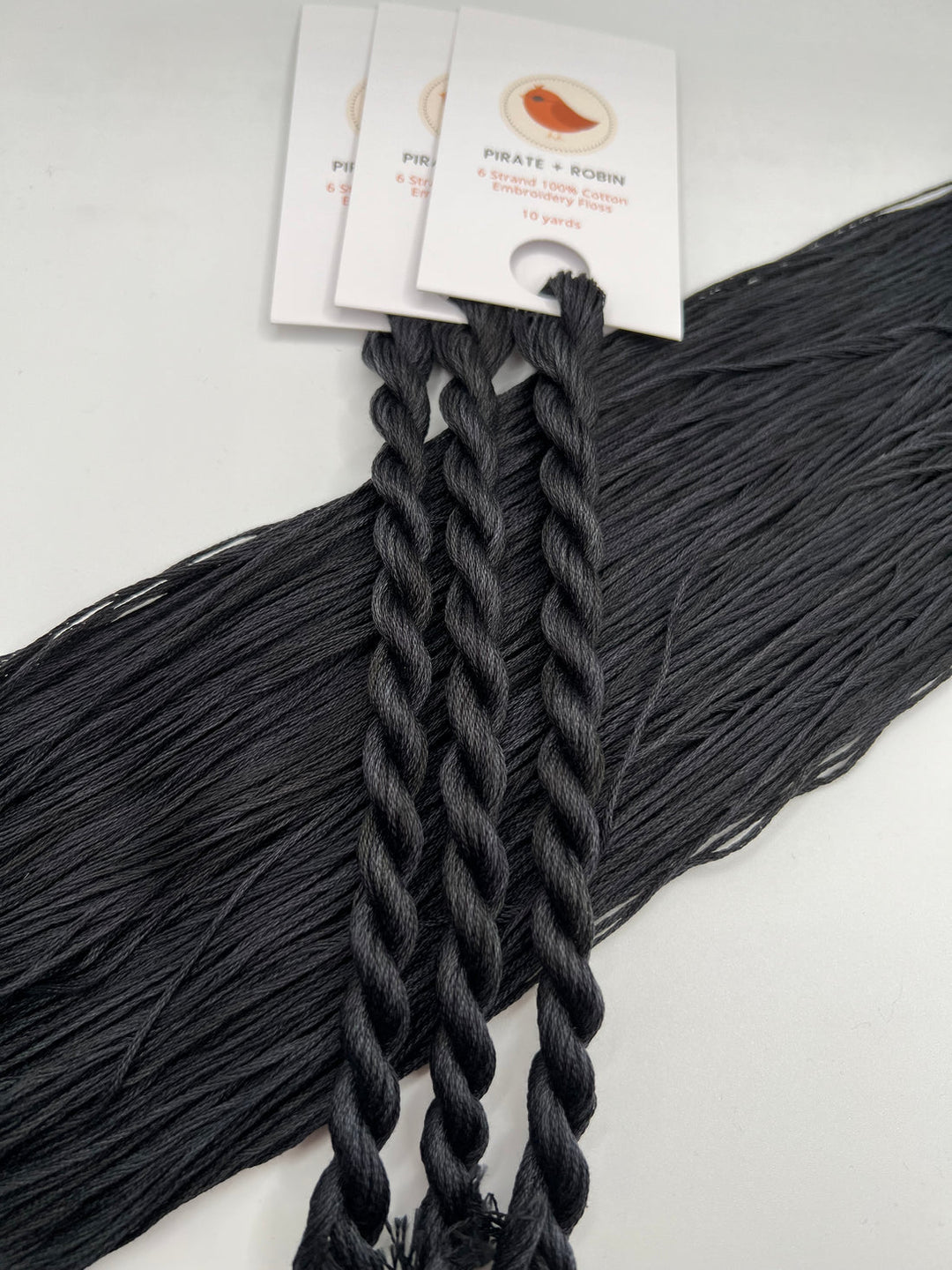 Black braided skeins of embroidery thread with brand labels on a white background