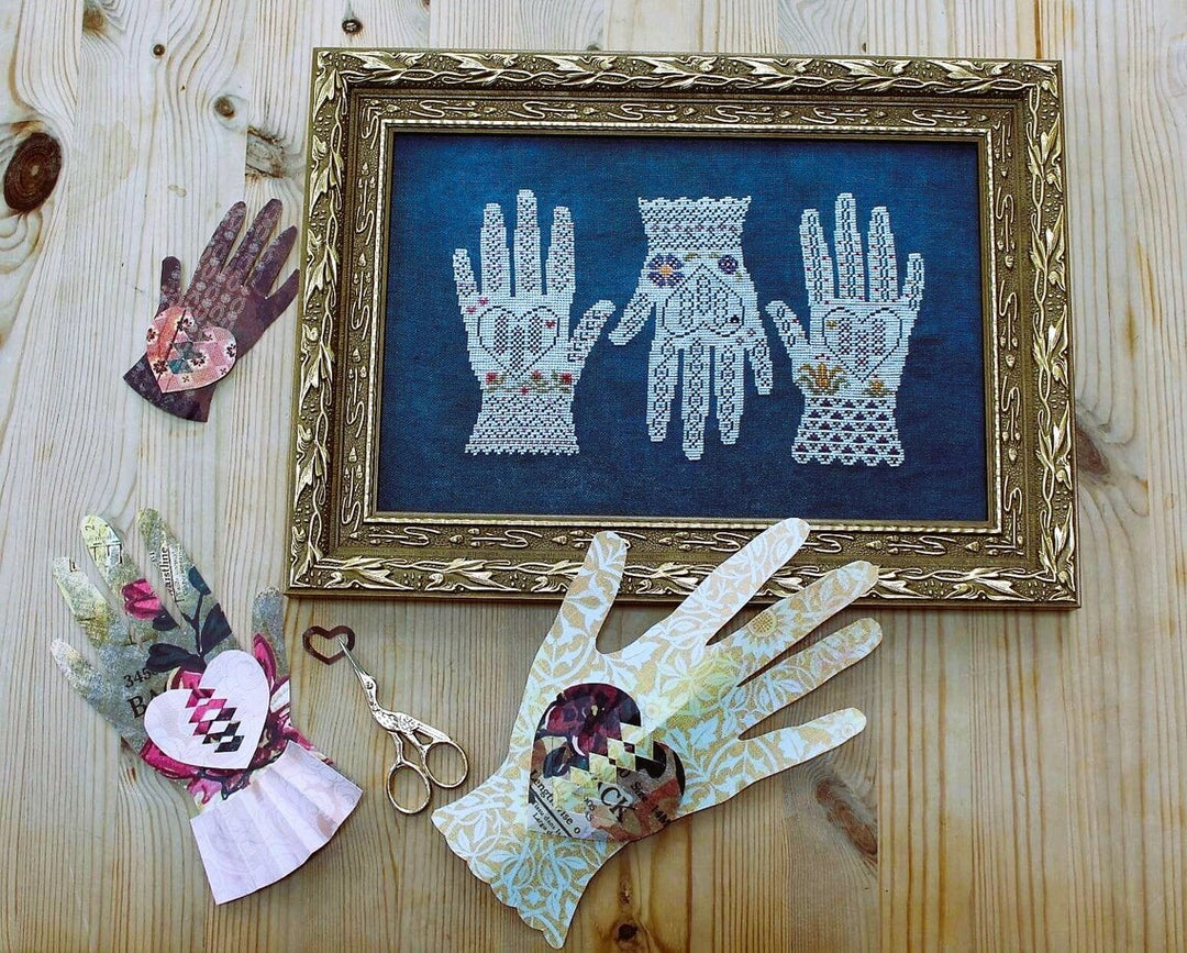 Decorative framed artwork of lace hands on a wooden surface with decorative gloves and scissors.