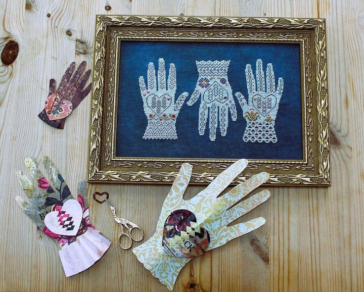 Decorative framed artwork of lace hands on a wooden surface with decorative gloves and scissors.