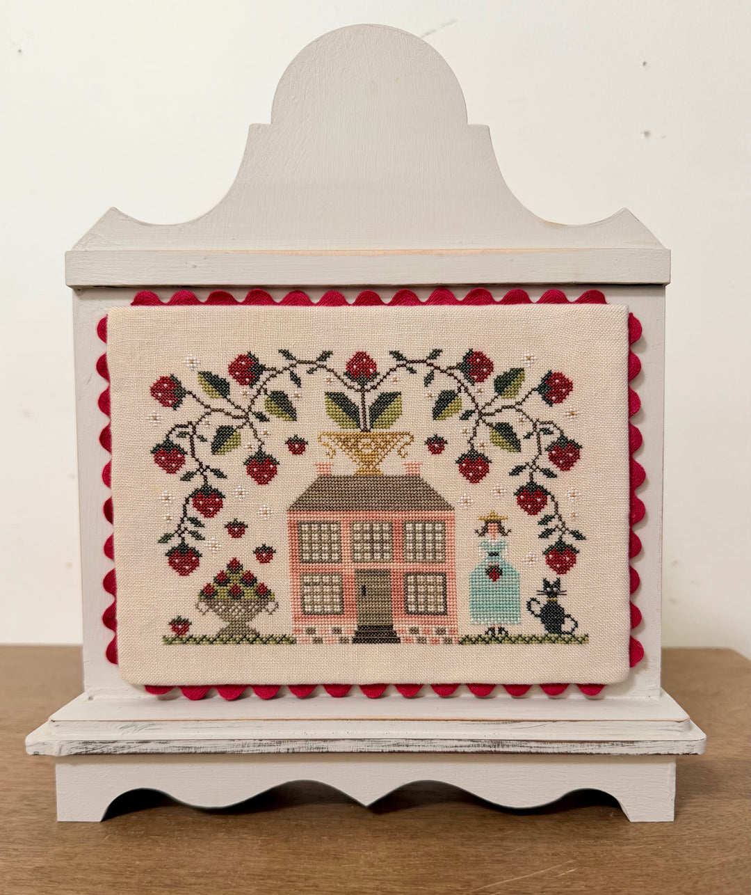 Decorative box with cross-stitched design featuring a house and people, on a white background.