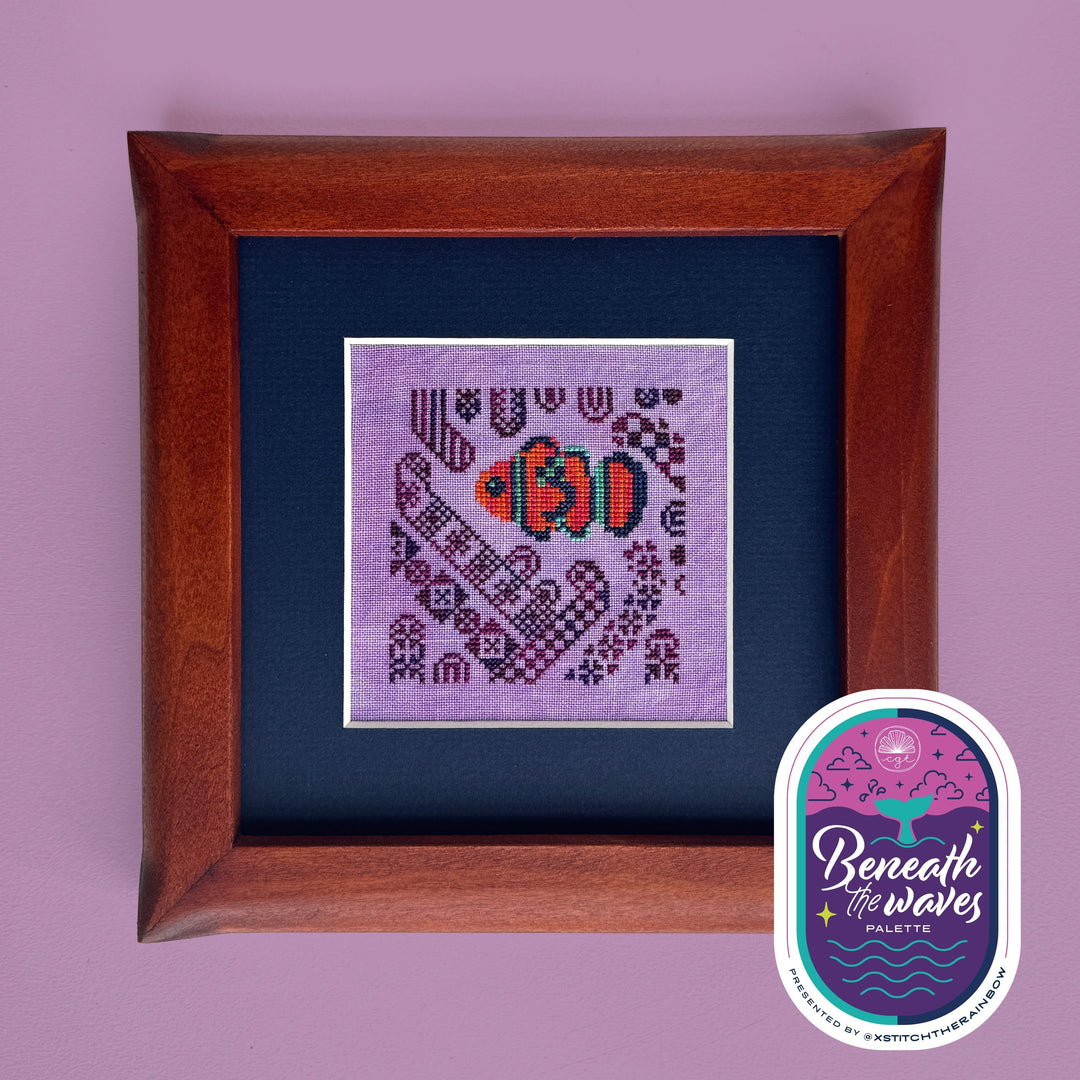 Framed cross-stitched fish design on purple fabric with 'Beneath the Waves' label.