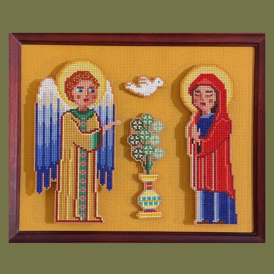 Embroidered picture of an angel and a woman with a dove and plant in the center, framed in brown.