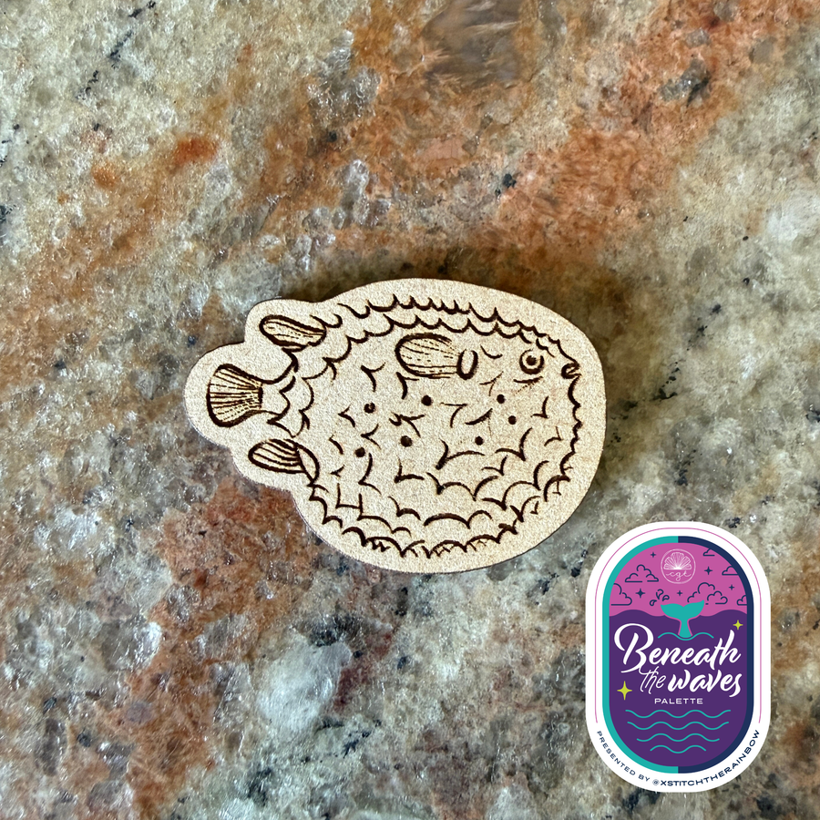 Wooden fish-shaped ornament on a textured stone surface with 'Beneath the Waves' palette logo.