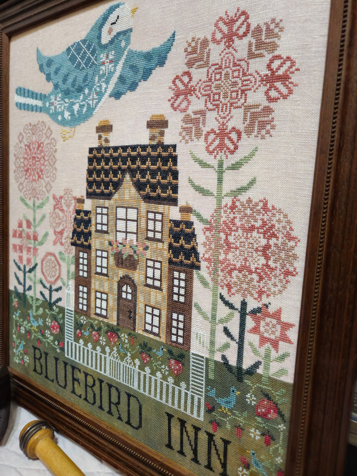 Embroidery of a house with flowers and birds, labeled 'Bluebird Inn'.