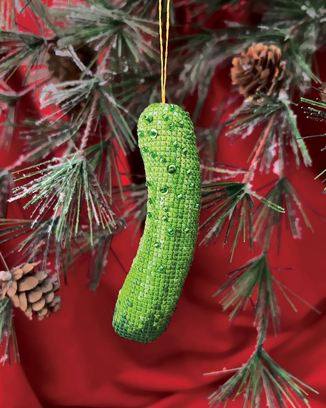 Green knitted pickle ornament hanging on a Christmas tree with red background