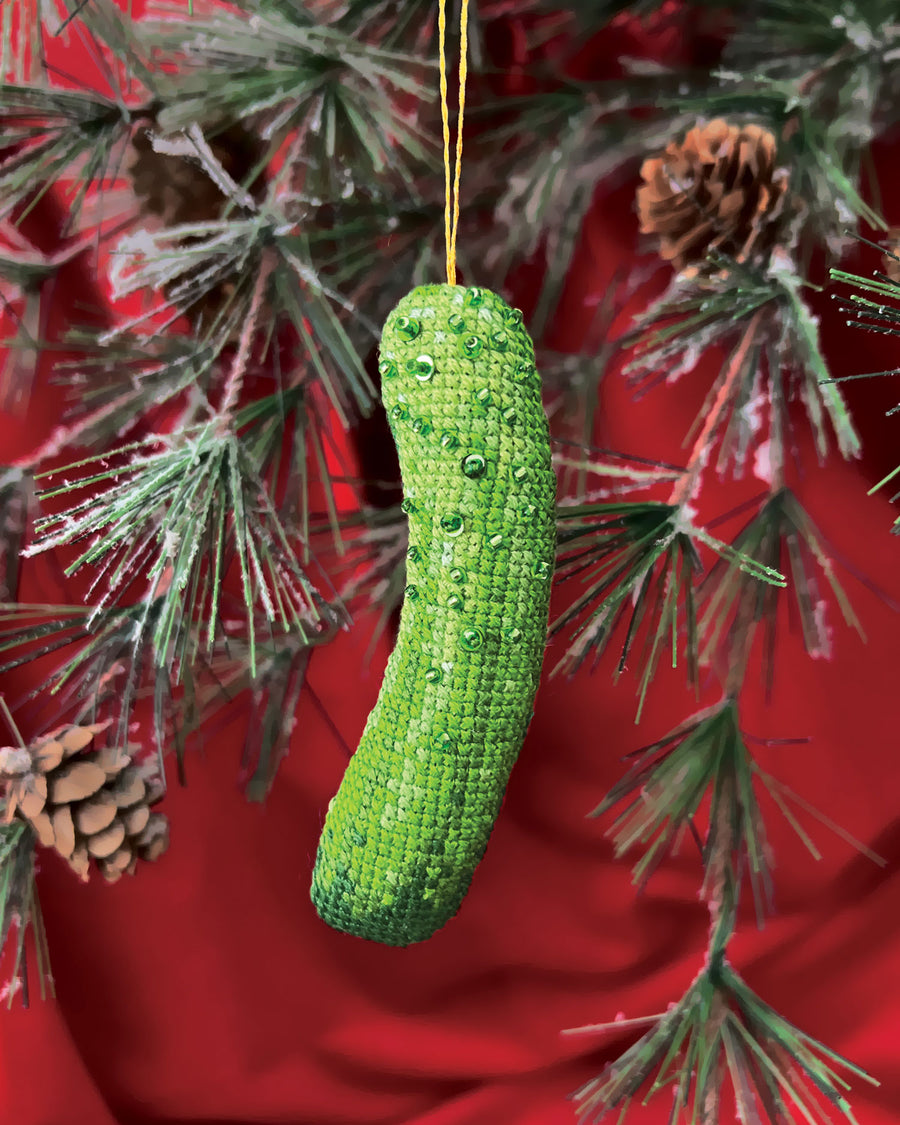 Green knitted pickle ornament hanging on a Christmas tree with red background