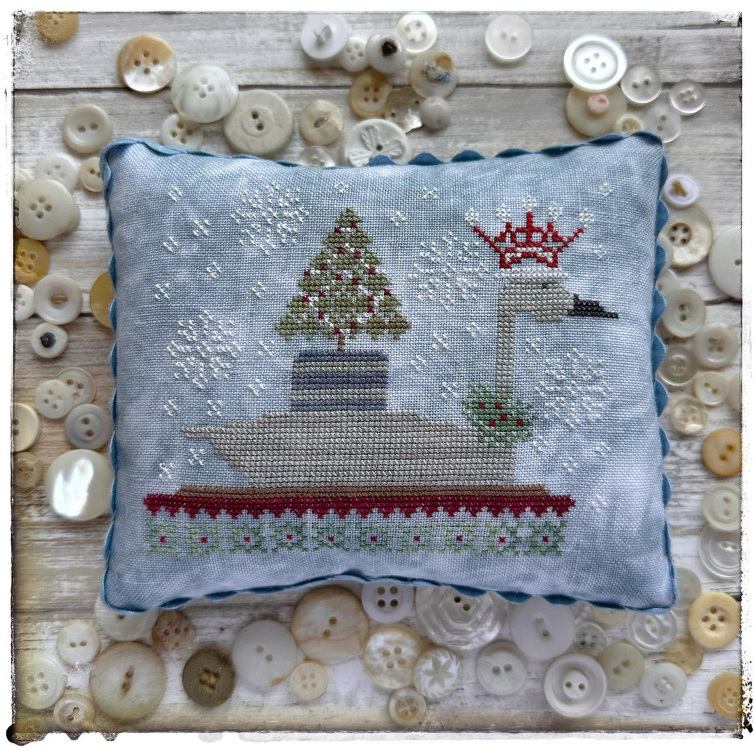 Cross-stitched pillow with a Christmas scene surrounded by buttons on a wooden surface