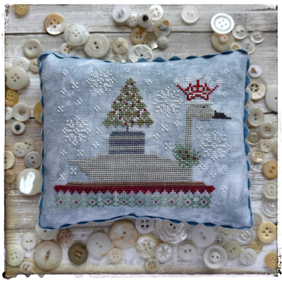 Cross-stitched pillow with a Christmas scene surrounded by buttons on a wooden surface