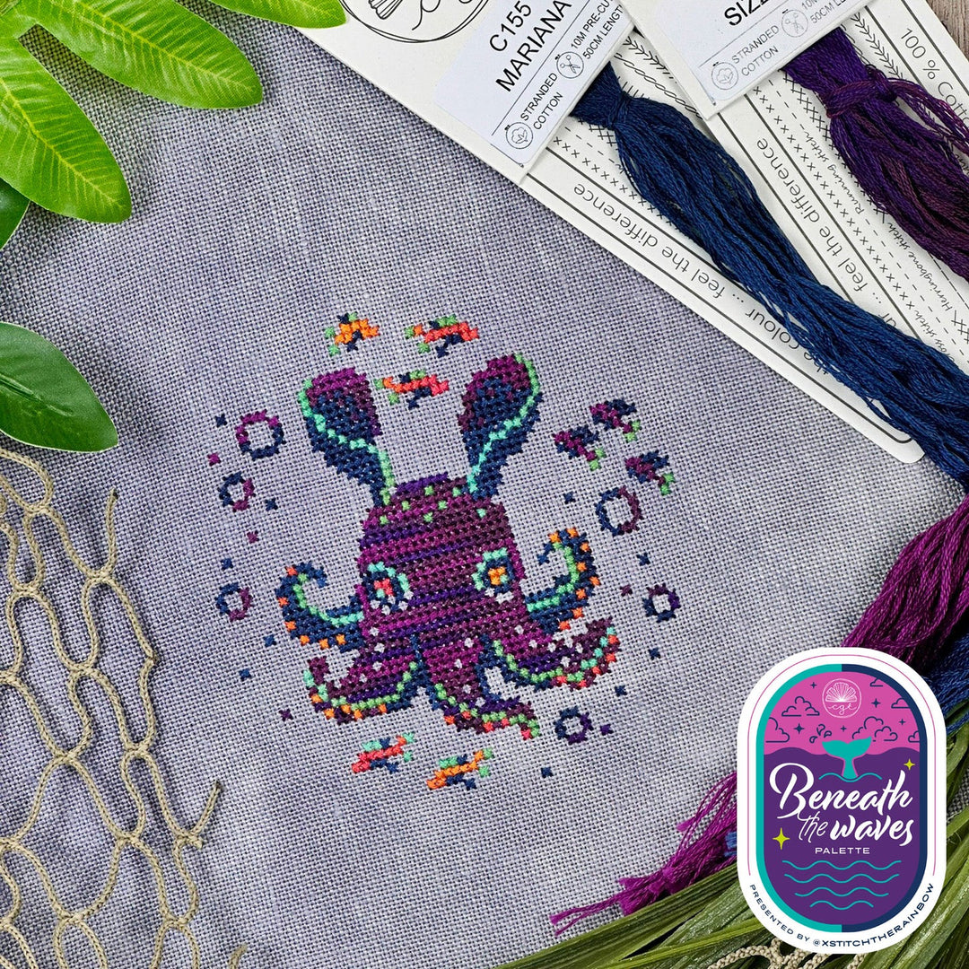 Cross-stitched octopus design on fabric with embroidery threads and 'Beneath the Waves' logo.