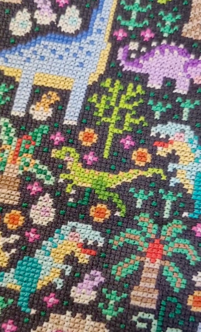 Cross-stitched pattern with colorful dinosaurs and plants on a black background