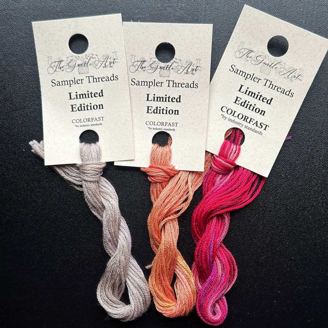 Three skeins of embroidery thread in pink, orange, and gray with labels on a dark background