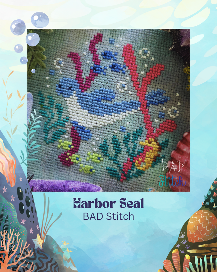 Cross-stitched harbor seal surrounded by underwater-themed decorations on a light blue background.