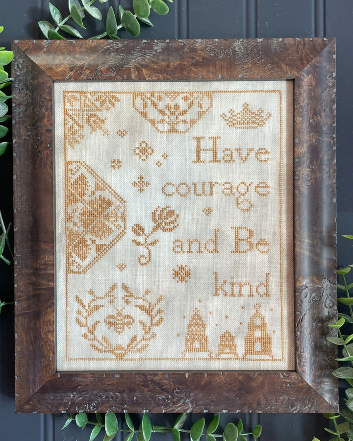 Framed cross-stitched artwork with have courage and be kind quote on a dark background