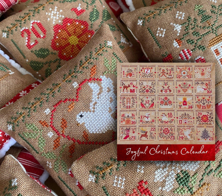 Cross-stitched fabric with festive designs and a Joyful Christmas Calendar card.