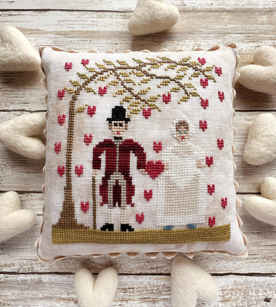 Decorative pillow with cross-stitched design of a man and tree on a wooden surface.