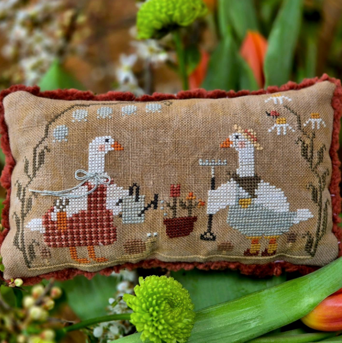 Decorative pillow with cross-stitched design of geese and flowers, surrounded by greenery.