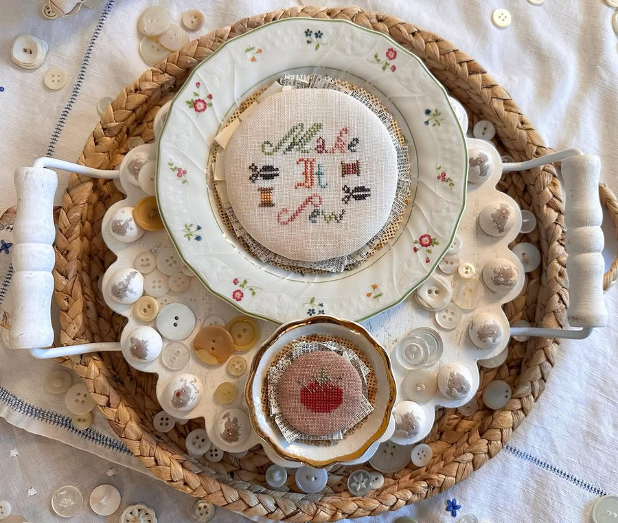 Decorative plate with embroidered designs and text, surrounded by buttons on a woven mat.