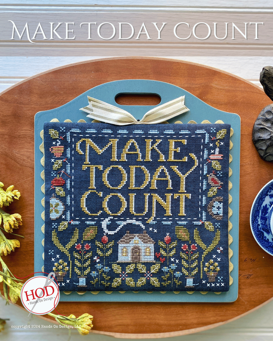 Cross-stitched pillow with 'MAKE TODAYCOUNT' text on a wooden surface, featuring the HOD logo.