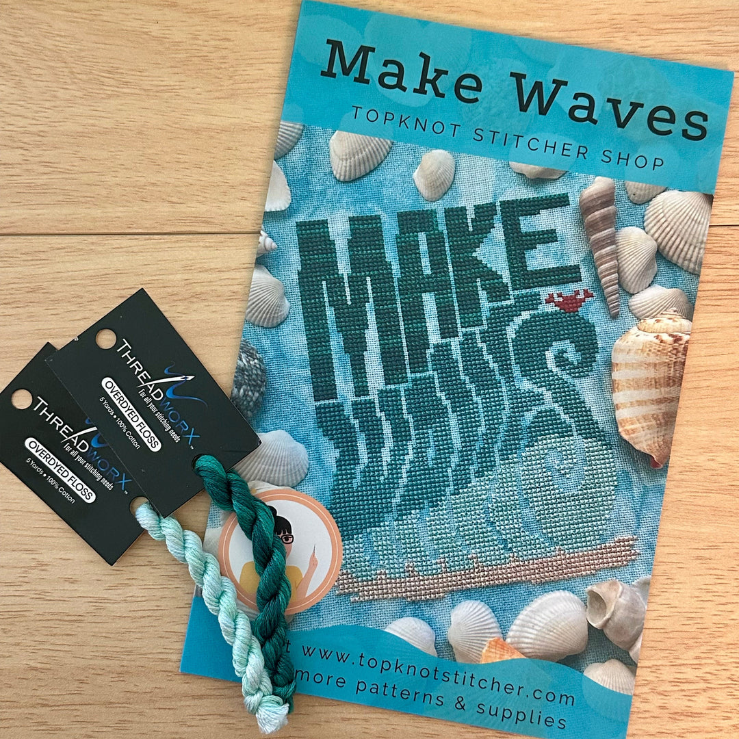 Cross-stitch pattern book titled 'Make Waves' with a two skeins of threadworx floss on a wooden surface