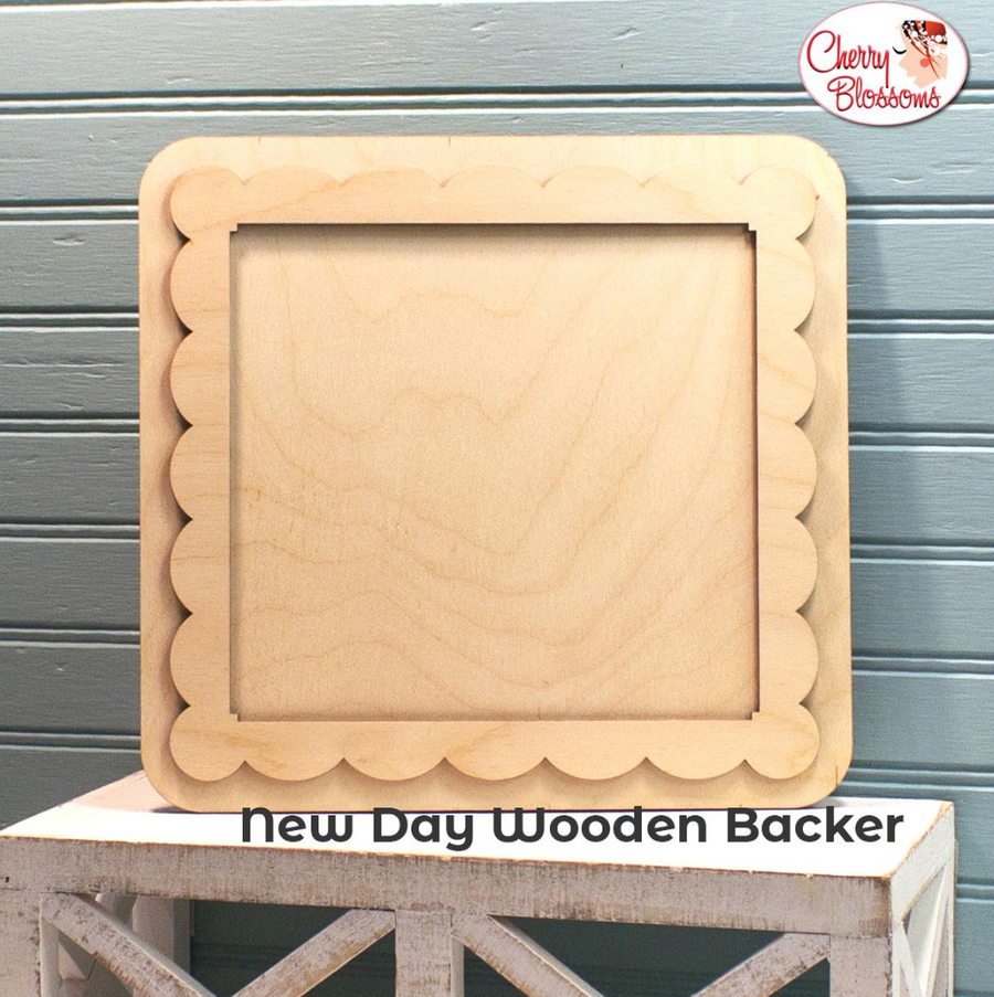 New Day Wooden Backer with scalloped cut-out frame on a wooden stand against a gray background.