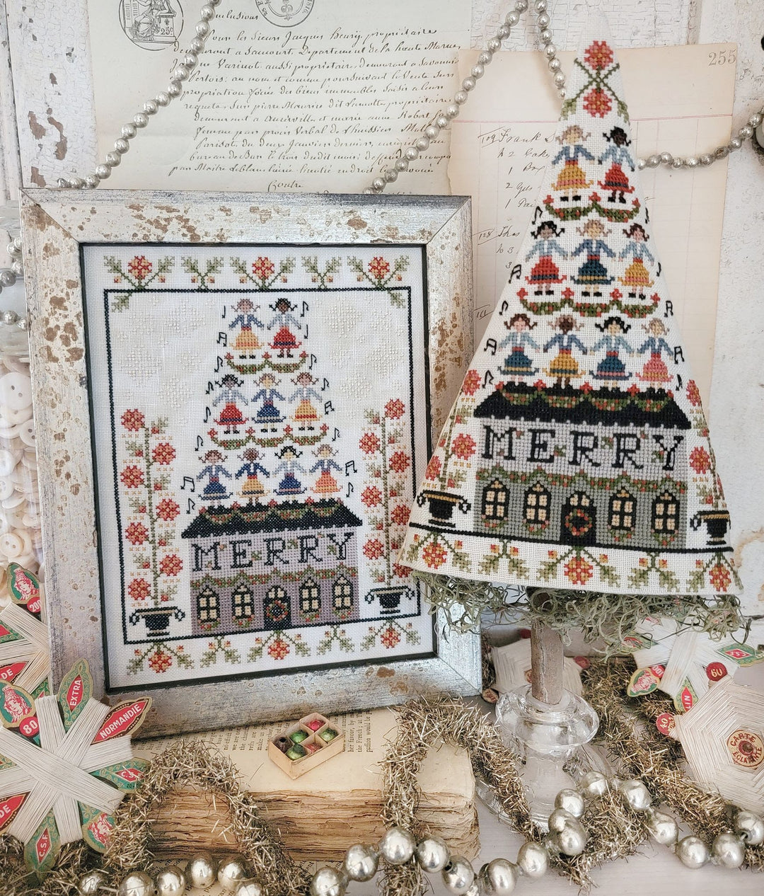 Decorative Christmas tree with cross-stitched design and framed cross-stitch pattern on a rustic background.