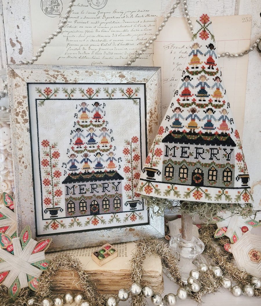 Decorative Christmas tree with cross-stitched design and framed cross-stitch pattern on a rustic background.