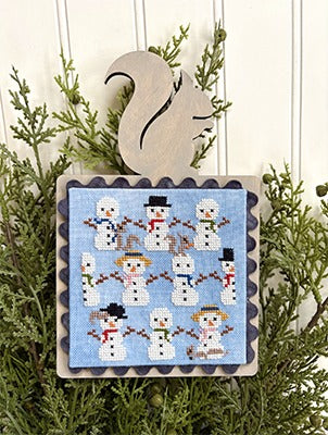 Decorative Christmas ornament with snowmen on a blue background, hanging on a green branch.