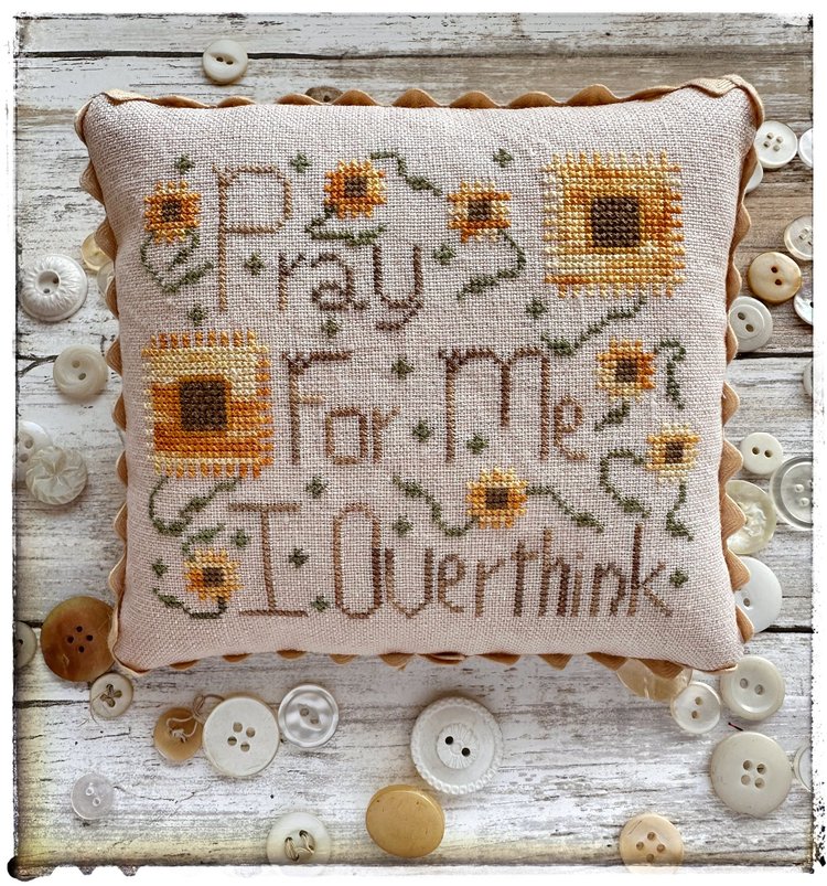 Decorative pillow with cross-stitched text and sunflowers on a wooden surface with buttons.