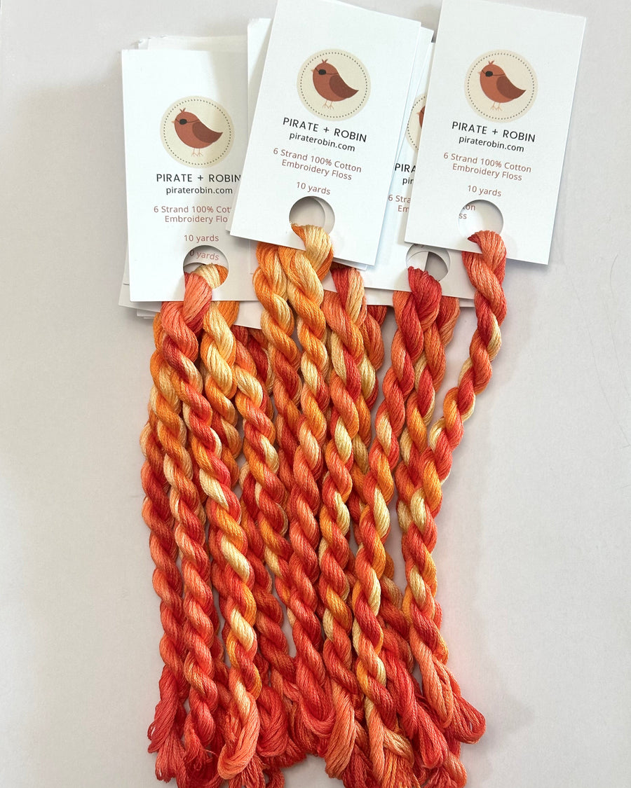 skeins of yarn in orange and red shades with tags on a white background